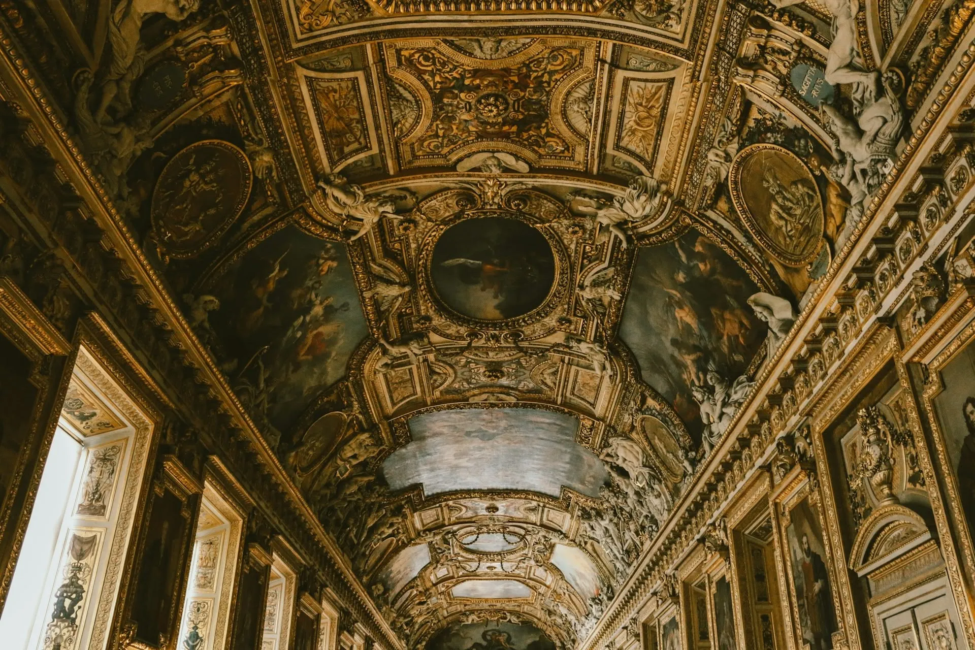 the louvre museum's ceiling, scattered with paintings and tinted golden and green.